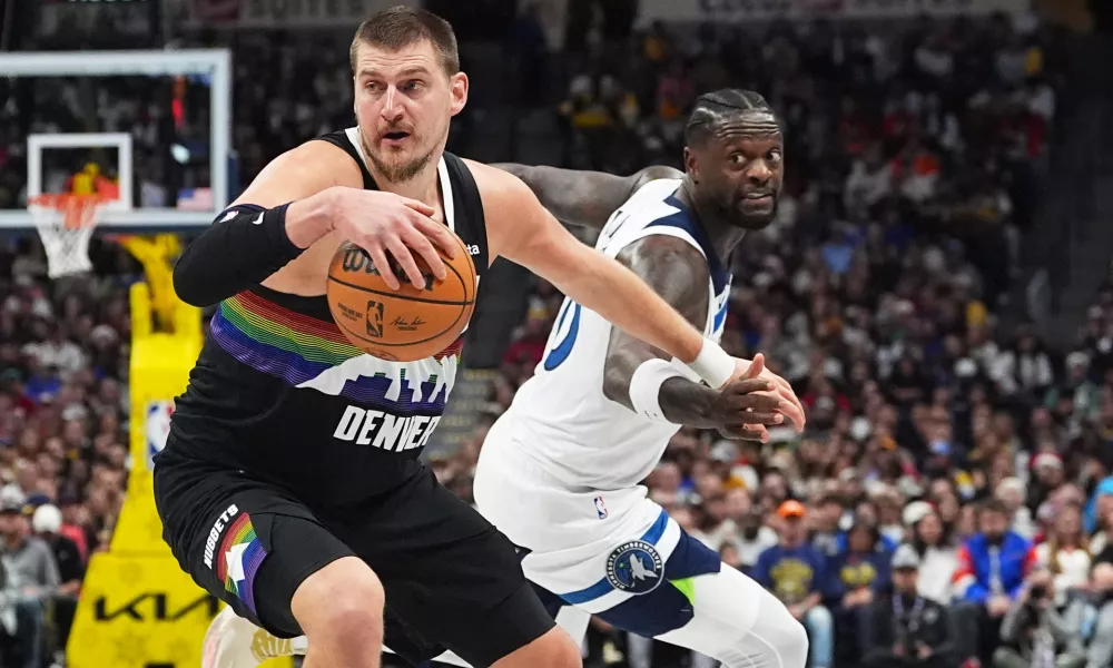 Denver Nuggets center Nikola Jokić, front, dribbles past Minnesota Timberwolves center Julius Randle in the first half of an NBA basketball game, Thursday, Dec. 25, 2025, in Denver. (AP Photo/David Zalubowski)