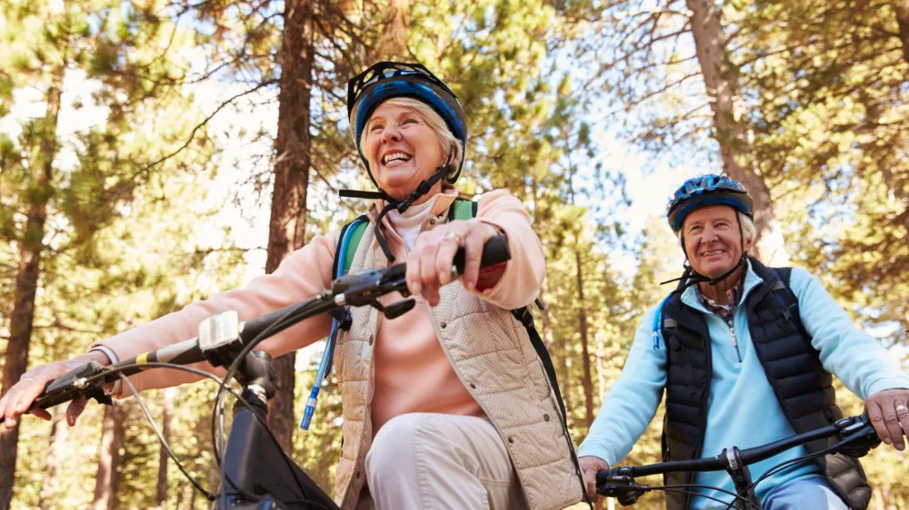 Senior couple mountain biking on a forest trail, low angle