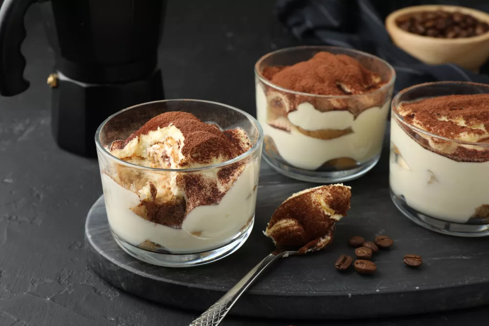 Delicious tiramisu in glasses, spoon and coffee beans on black table / Foto: Liudmila Chernetska