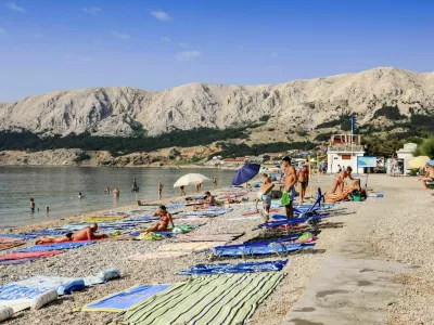 Baska, Krk, Croatia - July 6, 2012: People with their beach towels on the 1,800-meter-long Ba&scaron;ka beach (the Vela plaža, or "Great Beach") in this resort located on the SE of the Island of Krk.