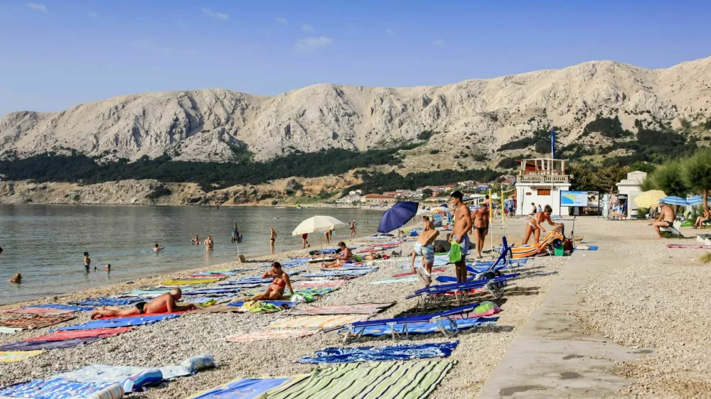 Baska, Krk, Croatia - July 6, 2012: People with their beach towels on the 1,800-meter-long Ba&scaron;ka beach (the Vela plaža, or "Great Beach") in this resort located on the SE of the Island of Krk.