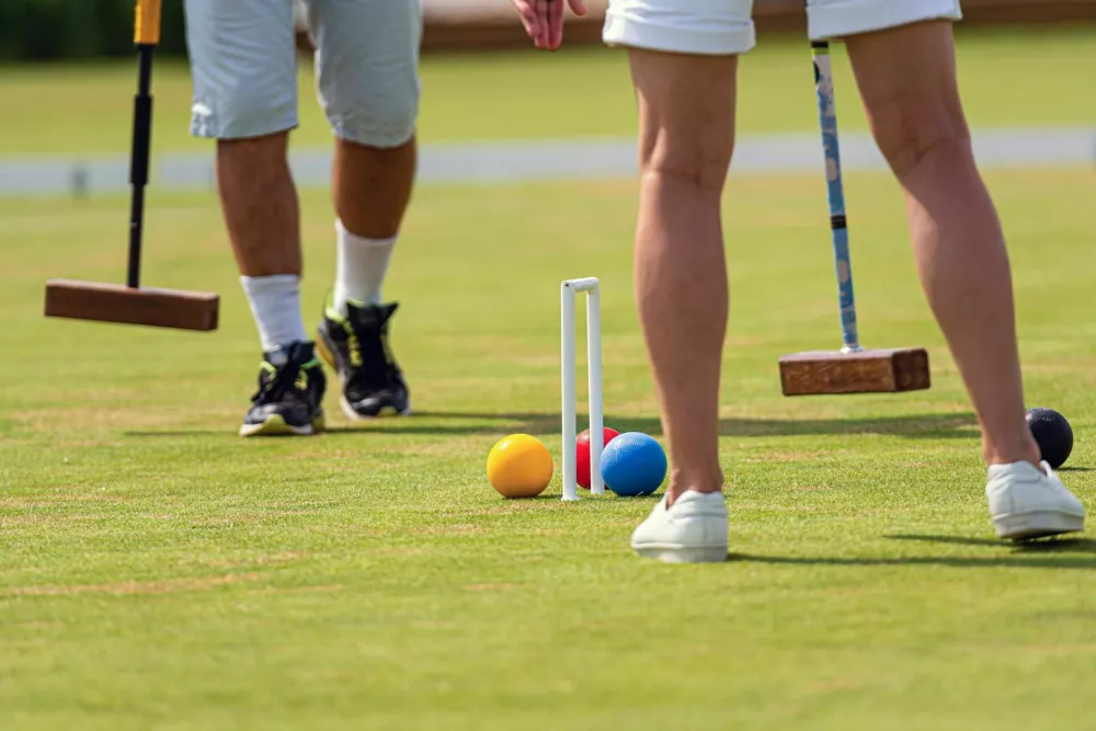 Two individuals engage in a lively croquet game on well-maintained grass during midday. / Foto: Askolds