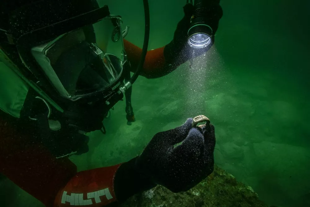 Story from Jam Press (Divers Ancient Ring)Pictured: The bronze signet at the time of its discovery on Antirhodos Royal Island's palace.PICTURES: Divers uncover lost 2,000-year-old ring inside Cleopatra's underwater 'sunken palace'Divers have discovered the first known ring depicting one of the Seven Wonders of the Ancient World.The extraordinary bronze signet shows the Lighthouse of Alexandria, which once towered over the Egyptian city and guided ships safely into its harbour.It was recovered from the remains of a submerged royal palace on Antirhodos, an island that formed part of Alexandria's ancient Royal Quarters before disappearing beneath the Mediterranean.The tiny treasure was found during underwater excavations led by French archaeologist Franck Goddio and the European Institute for Underwater Archaeology, as reported by NeedToKnow.Pictures from the expedition show divers exploring the murky ruins with torches before bringing the heavily corroded ring to the surface.Despite spending centuries underwater, its raised design remains visible and bears a striking resemblance to depictions of the lighthouse found on some second-century Roman coins.Experts say it is the first known bronze ring-signet to carry an image of the celebrated structure.The location of the find could make it even more significant.Archaeologists believe parts of the sprawling palace may once have housed administrative offices &ndash; potentially including officials responsible for running the lighthouse.Franck said: "The discovery of the ring-signet is even more important as it has been excavated in the legendary palace of the Island of Antirhodos, that once was a centre of power."The palace was witnessed by Greek geographer Strabo when he visited Egypt between 29 and 25BC.Archaeologists have now uncovered architectural remains covering several thousand square metres beneath the waves.The wider royal district was once associated with some of the ancient world's most famous figures, including Cleopatra VII, Julius Caesar and Mark Antony.Alexandria was founded by Alexander the Great in 331BC and later became the capital of Egypt under the Ptolemaic dynasty.Its enormous lighthouse was built on the island of Pharos during the third century BC and is thought to have stood more than 100 metres tall.For centuries, it was among the tallest man-made structures on Earth and helped sailors navigate the dangerous approach to the bustling port.But repeated earthquakes badly damaged the lighthouse, and it eventually vanished, leaving the Great Pyramid of Giza as the only surviving member of the traditional Seven Wonders.Large areas of ancient Alexandria's waterfront also sank following earthquakes, tidal waves, subsidence and changes in sea level.Some remains now lie as much as eight metres beneath the surface.Egypt's Minister of Tourism and Antiquities, Sherif Fathy, and his assistant, Dr Ahmed Rehema, visited the expedition's research vessel to see the newly discovered ring and watch the underwater work.The mission has also been examining other sites around Alexandria's Eastern Harbour, with archaeologists recovering pottery, glassware and everyday objects spanning centuries of the city's history.Researchers hope continued work at Antirhodos will reveal more about how the palace operated and the people who lived and worked at the heart of ancient Alexandria.The excavations are being undertaken by the European Institute for Underwater Archaeology in collaboration with Egypt's Ministry of Tourism and Antiquities and with support from the Hilti Foundation.The institute has been investigating Alexandria's submerged ruins since 1992.ENDSEDITOR'S NOTE: Non-Exclusive Licence: A non-exclusive licence has been obtained directly from the verified copyright holder. The copyright holder retains the ability to license the content elsewhere.,Image: 1141372708, License: Rights-managed, Restrictions: EDITOR'S NOTE: Non-Exclusive Licence: A non-exclusive licence has been obtained directly from the verified copyright holder. The copyright holder retains the ability to license the content elsewhere., Model Release: no / Foto: Profimedia