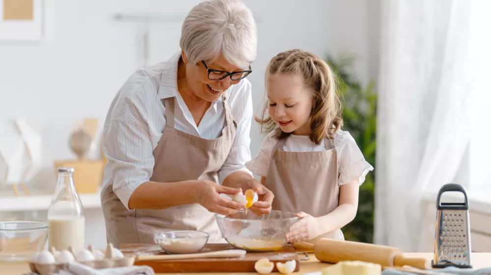 Happy loving family are preparing bakery together. Granny and child are cooking cookies and having fun in the kitchen.