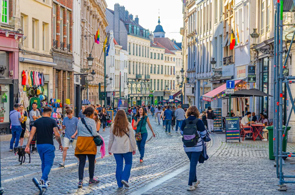 Brussels, Belgium, July 6, 2023: people tourists walking down pedestrian shopping street with many shops, stores, medieval houses and buildings in old town Brussels city historical center