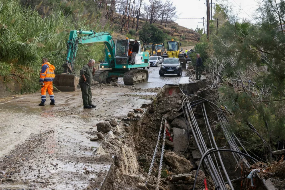 Workers stand by a partially collapsed road, after heavy rain continues to affect parts of Crete, prompting authorities to maintain severe weather warnings, near Ierapetra, Crete island, Greece, October 3, 2026. REUTERS/Stefanos Rapanis