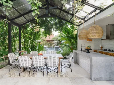 Open kitchen with empty dining room table and chairs outside, against green fresh plants on background