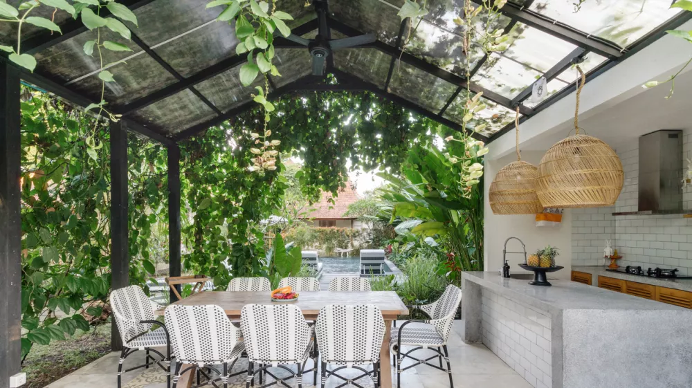 Open kitchen with empty dining room table and chairs outside, against green fresh plants on background