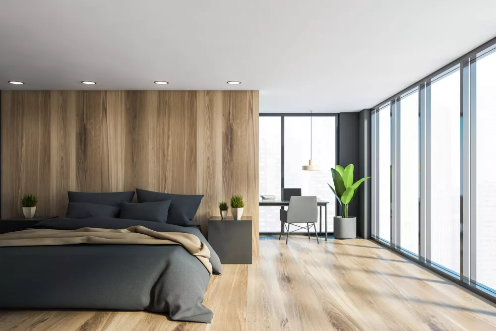 Interior of panoramic master bedroom with grey and wooden walls, king size bed with gray and beige blanket and home office corner. 3d rendering