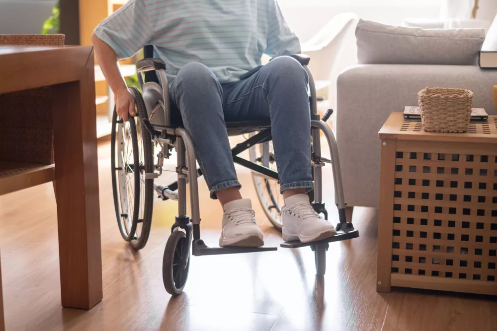 Person in a wheelchair navigating a modern living room, representing independence, mobility, and comfortable accessible housing for individuals with physical disabilities