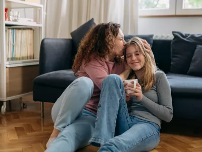 mother kiss her daughter while sitting on floor in living room