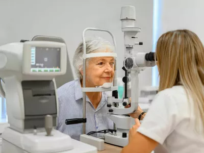 Female ophthalmologist examining senior woman's eyes with slit lamp while holding diagnostic lens in clinic / Foto: Moon Safari