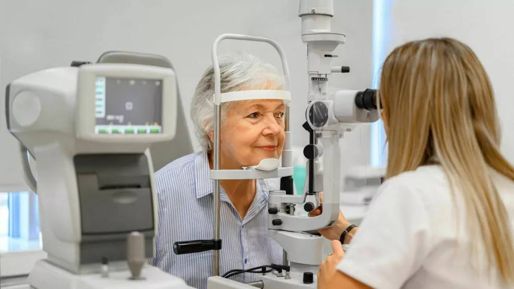 Female ophthalmologist examining senior woman's eyes with slit lamp while holding diagnostic lens in clinic / Foto: Moon Safari