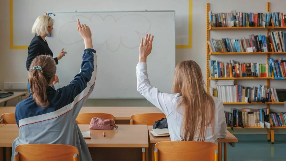 Two girl students during a classroom lecture, listening and communicating with a teacher. Education and learning concept.