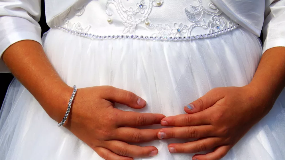 Cute little cild bridesmaid in white dress with hands on her belly