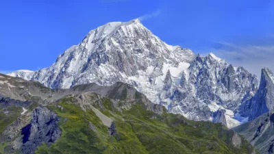 Panoramic view of snow-capped mountains and green valleys under a clear blue sky