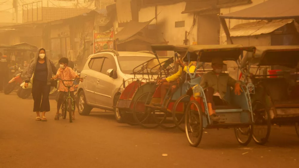 People wearing protective masks walk through the street as haze from wildfires shrouds the area in Palangka Raya, Central Kalimantan province, Indonesia, October 14, 2026. REUTERS/Arief Rahman Septian Prathama