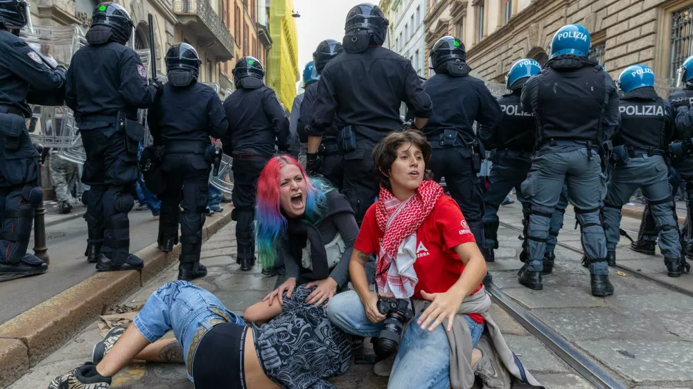 Demonstrators get shelter behind the police after clashes occurred during a protest against the high cost of living, in Milan, Italy, Saturday Oct. 17, 2026. (Stefano Porta/LaPresse via AP)