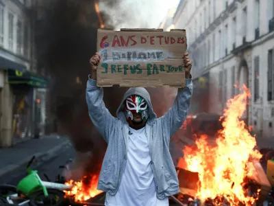 A person wearing a mask holds a placard reading "6 years of education, 1 diploma, 9 rejections a day" in front of burning flames, the day after a national day of demonstrations against the cost of living and rising fuel prices, in Paris, France, October 18, 2026. REUTERS/Abdul Saboor