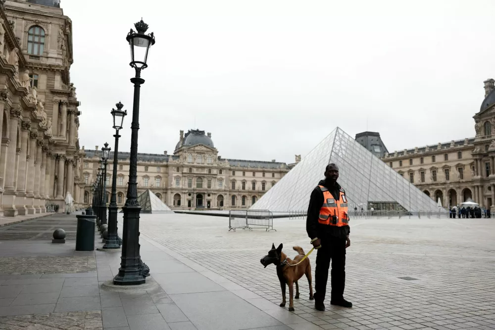A security employee with a dog stands near the glass Pyramid of the Louvre Museum as the museum remains closed the day after a spectacular jewel heist by thieves who broke into the landmark by using a crane and smashing an upstairs window, stealing priceless jewelry from an area that houses the French crown jewels before escaping on motorbikes, in Paris, France, October 20, 2025. REUTERS/Benoit Tessier