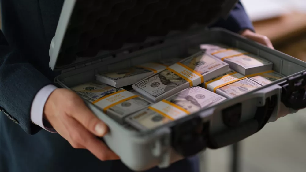 Businessman in suit holding suitcase full of currency money closeup. Profitable financial deals concept
