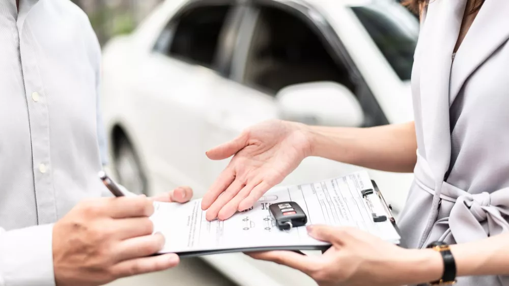 Automotive business, car sale or rental concept: Happy customer with car dealer agent making deal and signing on agreement document contract in auto showroom or car dealer office.