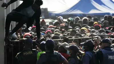 FILE - A Malawian migrant jumps over a barricade as the police officer manage the queue for their deportation at a temporary centre, in Durban, South Africa, Thursday, June 18, 2026. (AP Photo/Themba Hadebe, File)