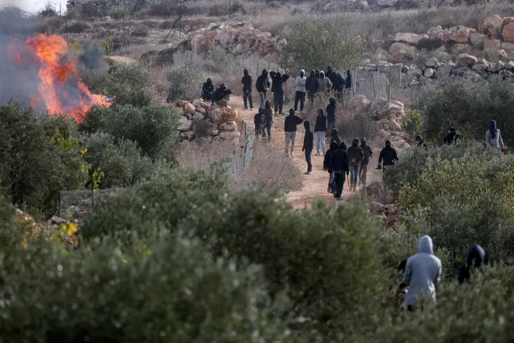 FILE PHOTO: Palestinians look towards Israeli settlers standing near a fire amid clashes during olive harvest in Abu Falah near Ramallah in the Israeli-occupied West Bank, October 16, 2026. REUTERS/Ammar Awad/File Photo