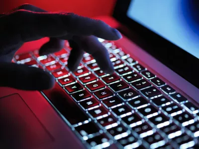 A hand types on a backlit laptop keyboard, illuminated with red and white lights, with a blurred background.