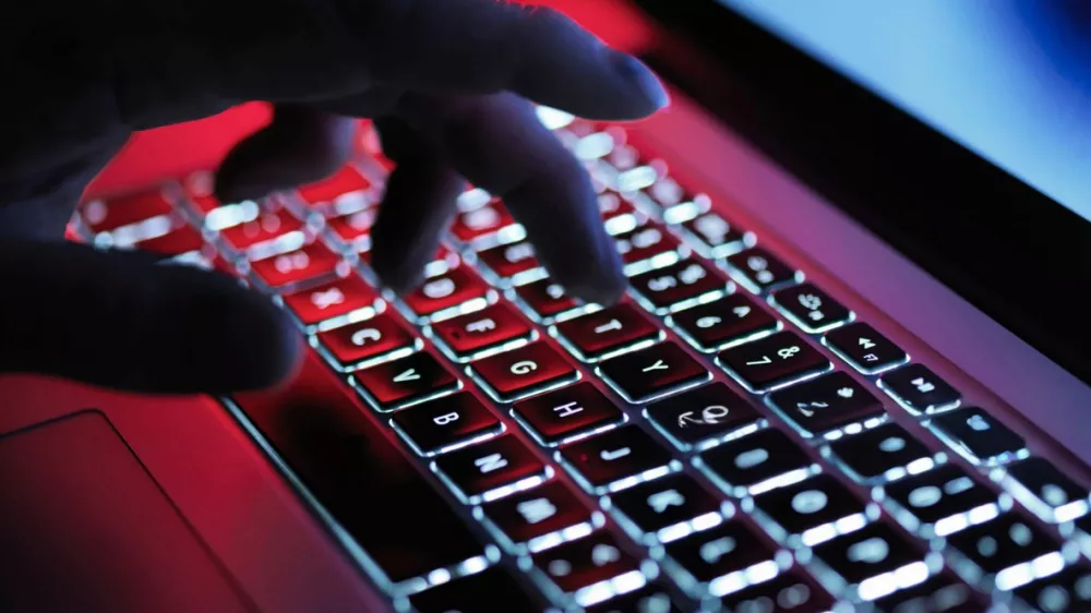 A hand types on a backlit laptop keyboard, illuminated with red and white lights, with a blurred background.