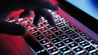 A hand types on a backlit laptop keyboard, illuminated with red and white lights, with a blurred background.