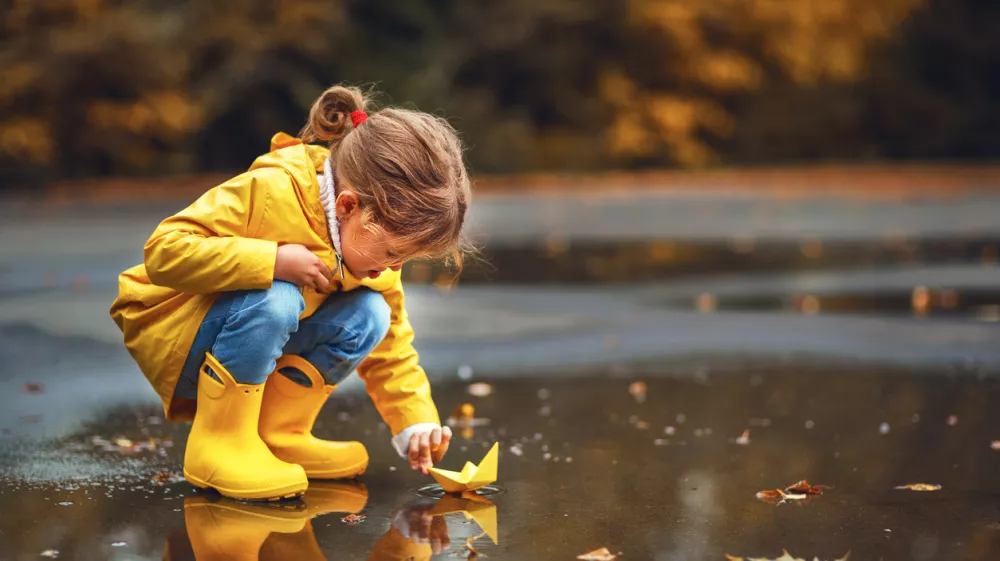 happy child girl with umbrella and paper boat in a puddle in autumn on nature