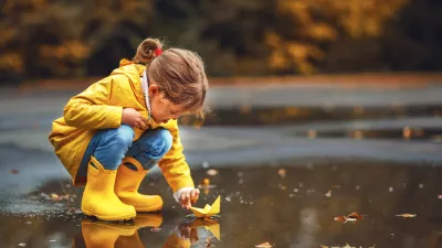 happy child girl with umbrella and paper boat in a puddle in autumn on nature