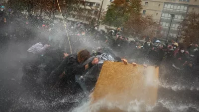 Protesters take cover behind a plywood board as French riot police use a water canon amid clashes during a demonstration organised by labour unions in Paris as part of nationwide protests called by the "Yellow Vests" movement joined by French high school and university students against the cost of living and rising fuel prices, in France, October 24, 2026. REUTERS/Pedro Nunes