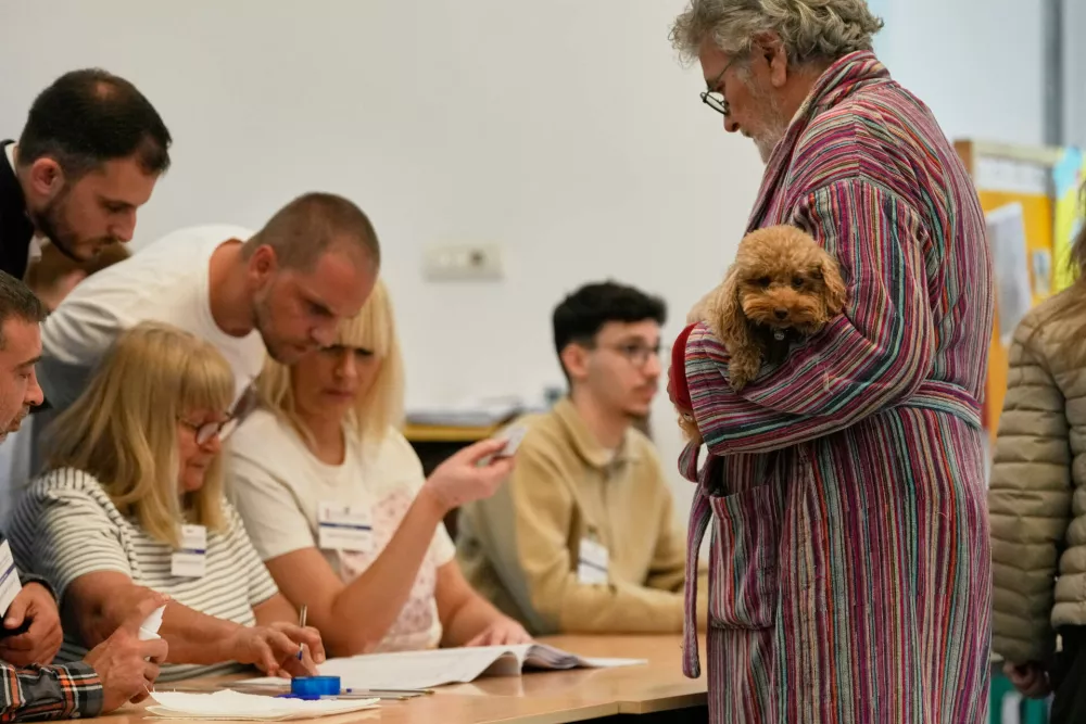 A man holding a dog waits to receive the ballot paper before voting in a parliamentary election in Belgrade, Serbia, Sunday, Oct. 25, 2026. (AP Photo/Darko Vojinovic)