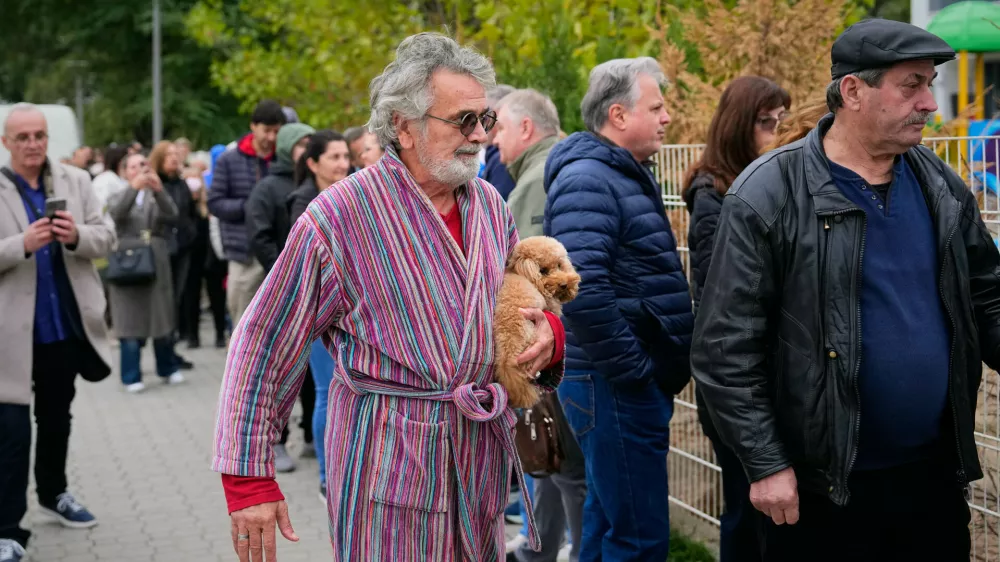 A man holds a dog while arriving at a polling station to vote in a parliamentary election in Belgrade, Serbia, Sunday, Oct. 25, 2026. (AP Photo/Petr David Josek)