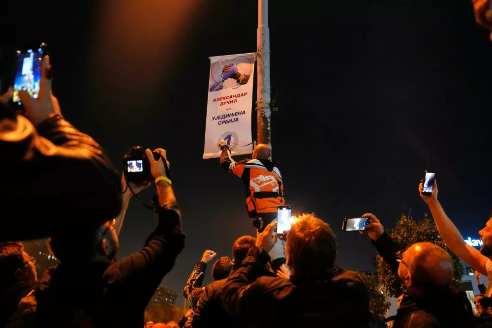 People shoot photos and video on their mobile phones as a man tears down a poster of Aleksandar Vucic's, right-wing Serbian Progressive Party (SNS) after he conceded defeat in the parliamentary election in Belgrade, Serbia, Sunday, Oct. 25, 2026. (AP Photo/Petr David Josek)