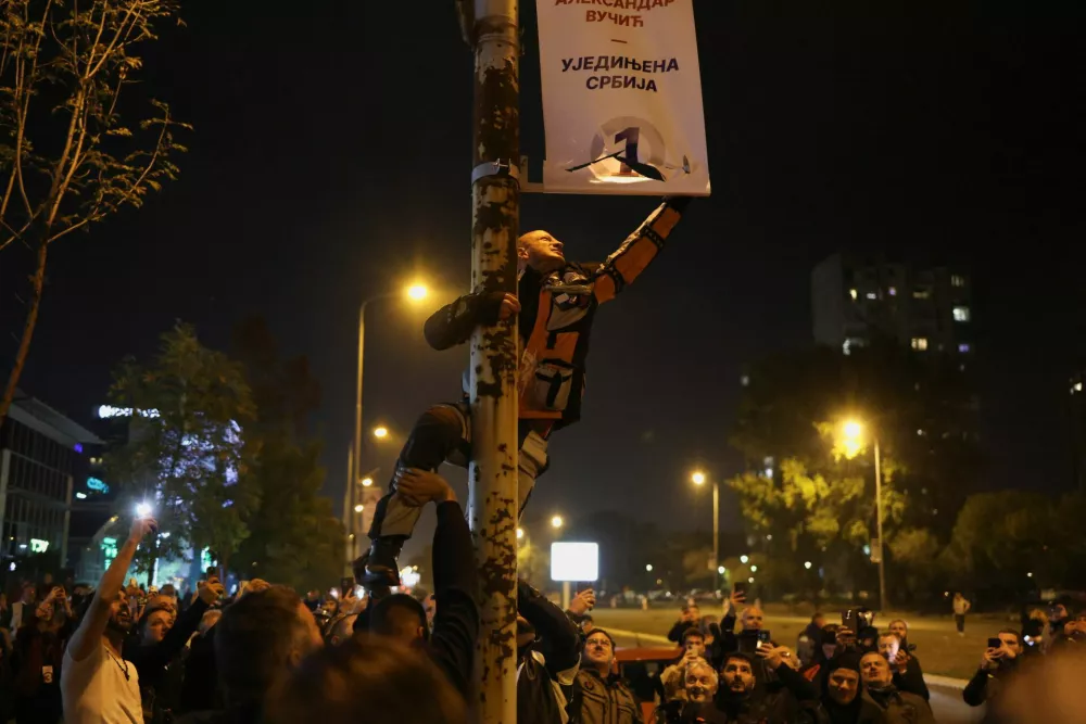 A supporter of the electoral list "Student List - Students Win" damages a banner of Serbia's former President and the ruling Serbian Progressive Party (SNS) prime ministerial candidate Aleksandar Vucic as others celebrate following the first results of the parliamentary election in Belgrade, Serbia, October 25, 2026. REUTERS/Marko Djurica