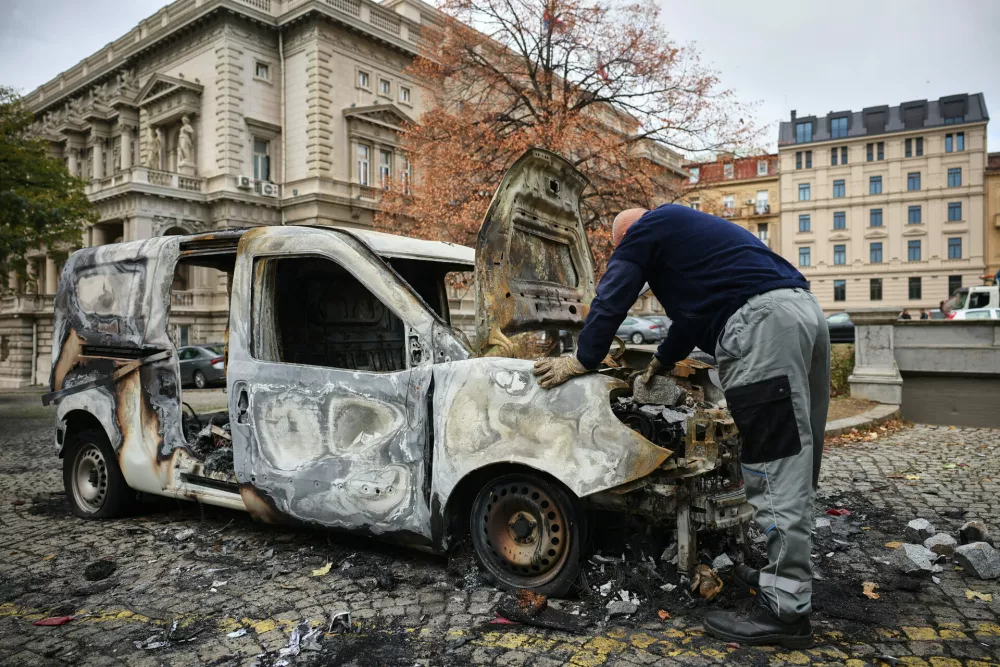 A man examines a burnt-out vehicle in a park used as a camp by supporters of the right-wing Serbian Progressive Party (SNS) where tents and vehicles were set on fire by celebrating crowds after Aleksandar Vucic, the party leader conceded defeat in the parliamentary election, held on Sunday, in Belgrade, Serbia, Monday, Oct. 26, 2026. (AP Photo/Armin Durgut)