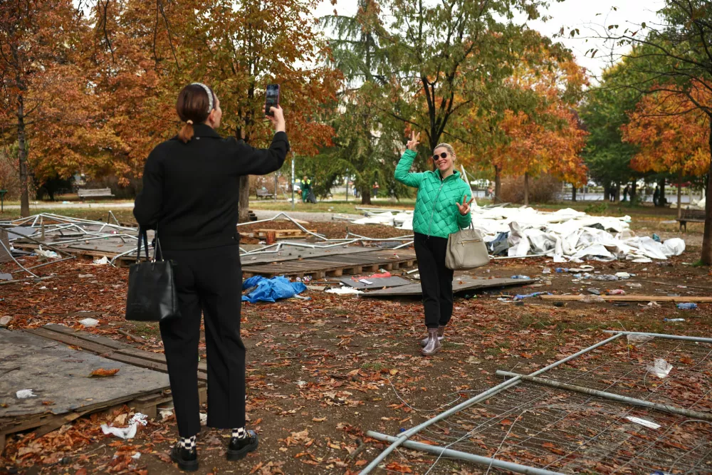Women take photos backdropped by debris in a park used as a camp by supporters of the right-wing Serbian Progressive Party (SNS) where tents and vehicles were set on fire by celebrating crowds after Aleksandar Vucic, the party leader conceded defeat in the parliamentary election, held on Sunday, in Belgrade, Serbia, Monday, Oct. 26, 2026. (AP Photo/Armin Durgut)
