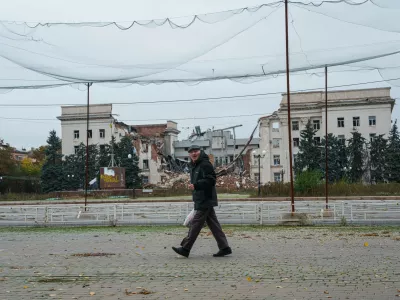 A man walks beneath anti-drone nets stretched over a street in front of a destroyed regional administration building during a local ceasefire linked to efforts to evacuate residents of Oleshky, in Kherson, Ukraine, Tuesday, Oct. 27, 2026. (AP Photo/Evgeniy Maloletka)