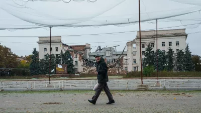 A man walks beneath anti-drone nets stretched over a street in front of a destroyed regional administration building during a local ceasefire linked to efforts to evacuate residents of Oleshky, in Kherson, Ukraine, Tuesday, Oct. 27, 2026. (AP Photo/Evgeniy Maloletka)
