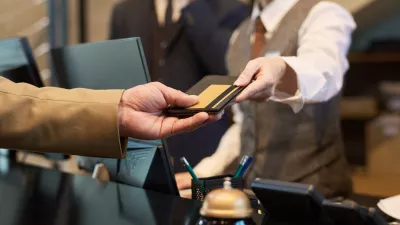 Receptionist taking credit card from guest at hotel reception for transaction processing. Elegant setup with polished service tools like bell and pen holder visible on counter