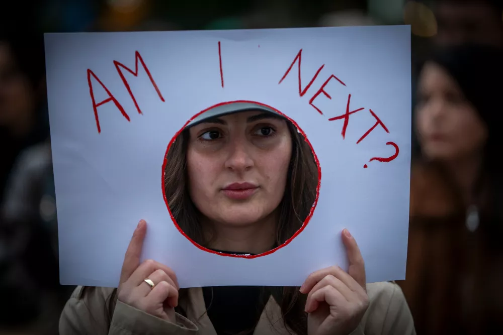 A woman holds a sign "Am I Next" as thousands of people gather in Kosovo's capital to protest the killing of a Kosovo-American woman, Arlinda Zekaj, whose death sparked public outrage and renewed calls for accountability over violence against women in capital Pristina, Kosovo, on Wednesday, Oct.28, 2026. (AP Photo/Visar Kryeziu)