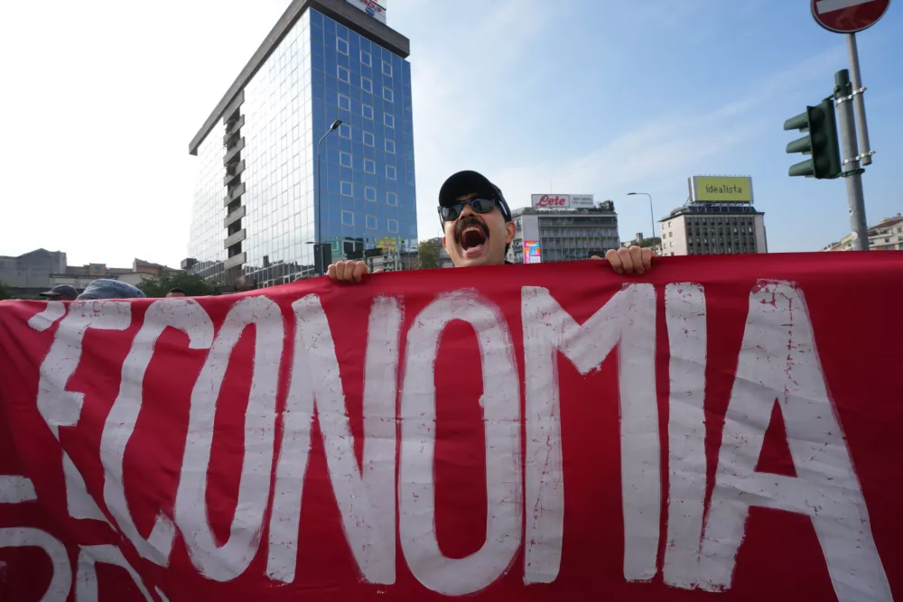 A demonstrator shouts slogans while holding a banner reading "Economy" during a nationwide general strike called by grassroots unions to protest rising living costs, low wages and military spending in Milan, Italy, Friday, Oct. 30, 2026. (AP Photo/Antonio Calanni)