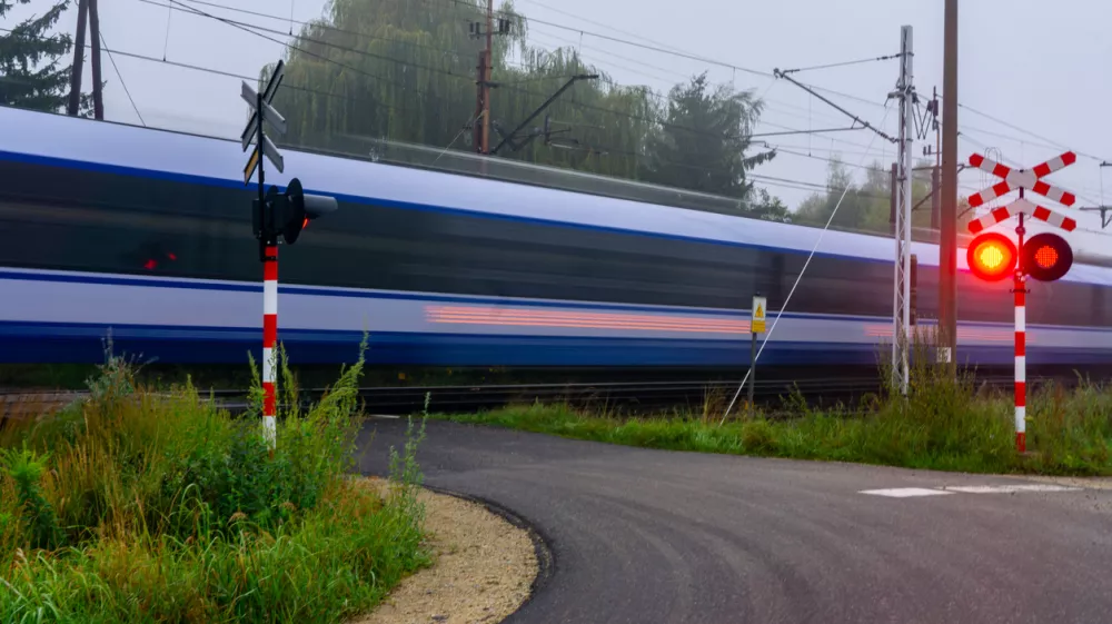 Passenger train passes railway crossing with red warning light, long exposure, motion blur, rail transport, safety, railway infrastructure, travel.